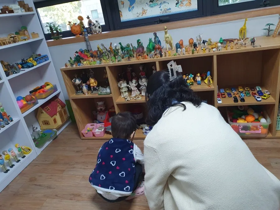 장난감 선반 앞에서 아이와 어른이 함께 놀잇감을 고르는 모습